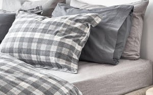 Flannel bedding gray with plaid. Pillows sitting on a bed.