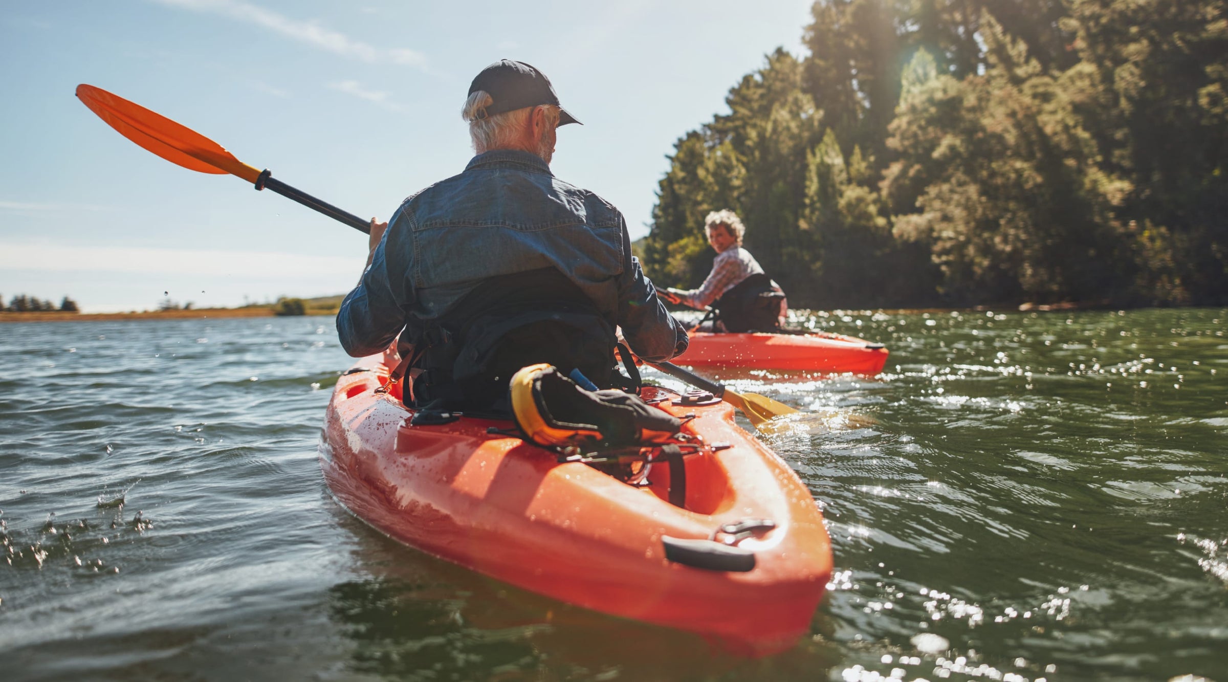 A middle age couple kayaking on a lake. There are trees in the background.